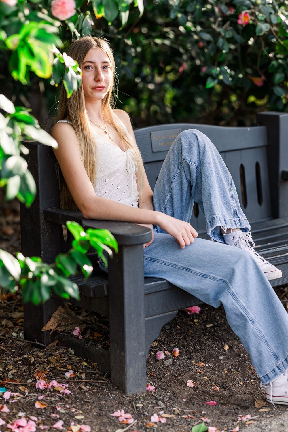 White top and jeans casual look on wooden bench surrounded by greenery and pink flowers in garden setting.