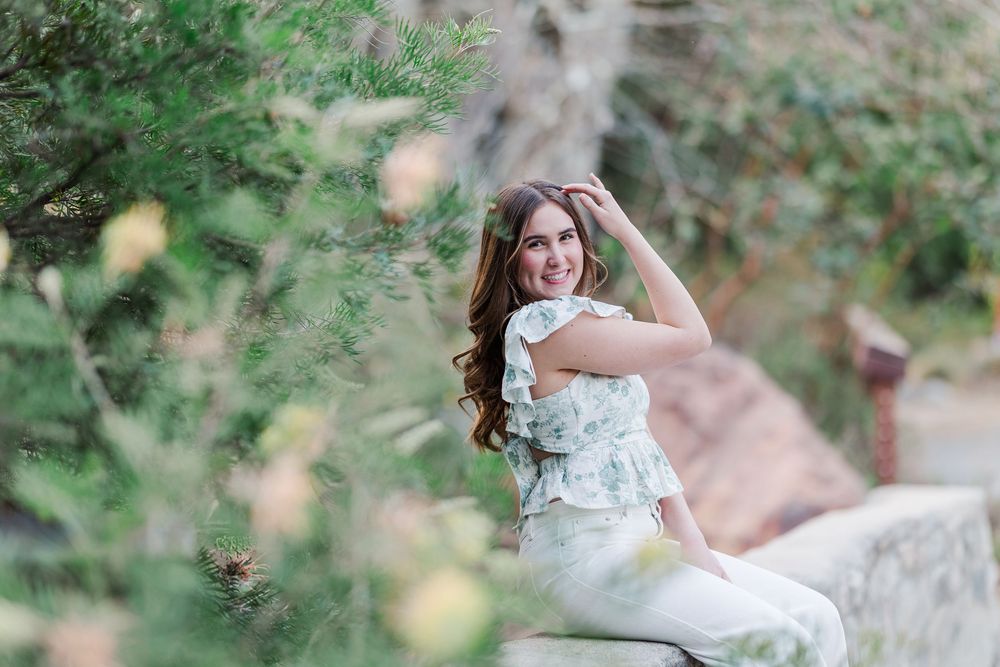 Elegant bride in white lace dress poses outdoors on rock with soft blurred natural background.