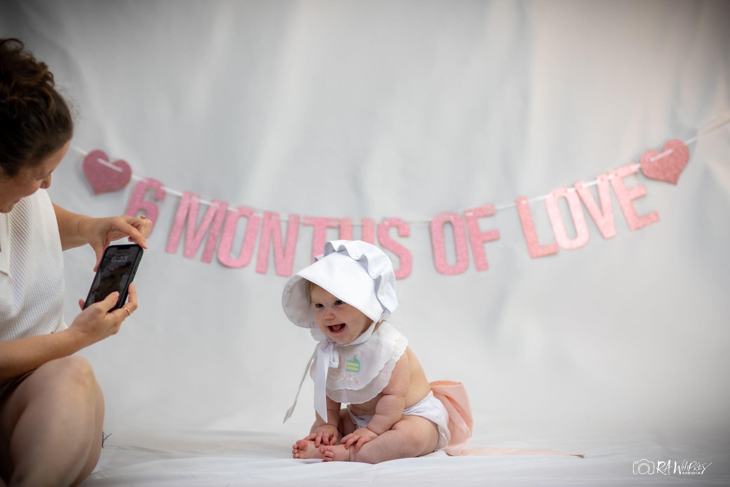 Baby milestone photoshoot setup with pink banner and white backdrop.