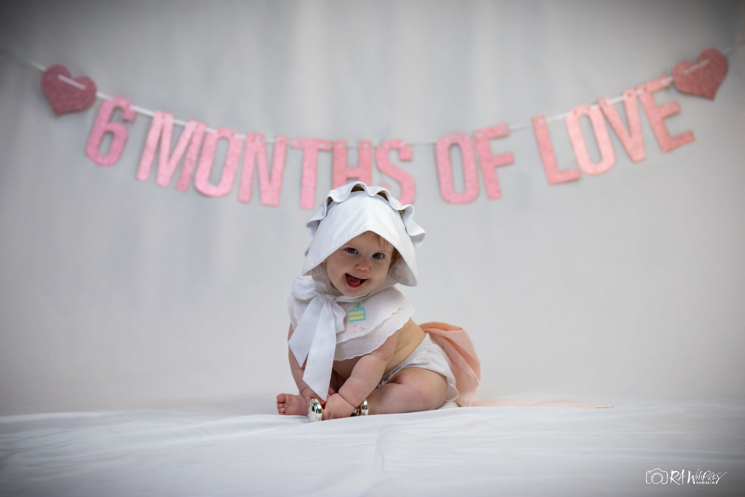 Six month milestone celebration setup with pink lettered banner against white background.