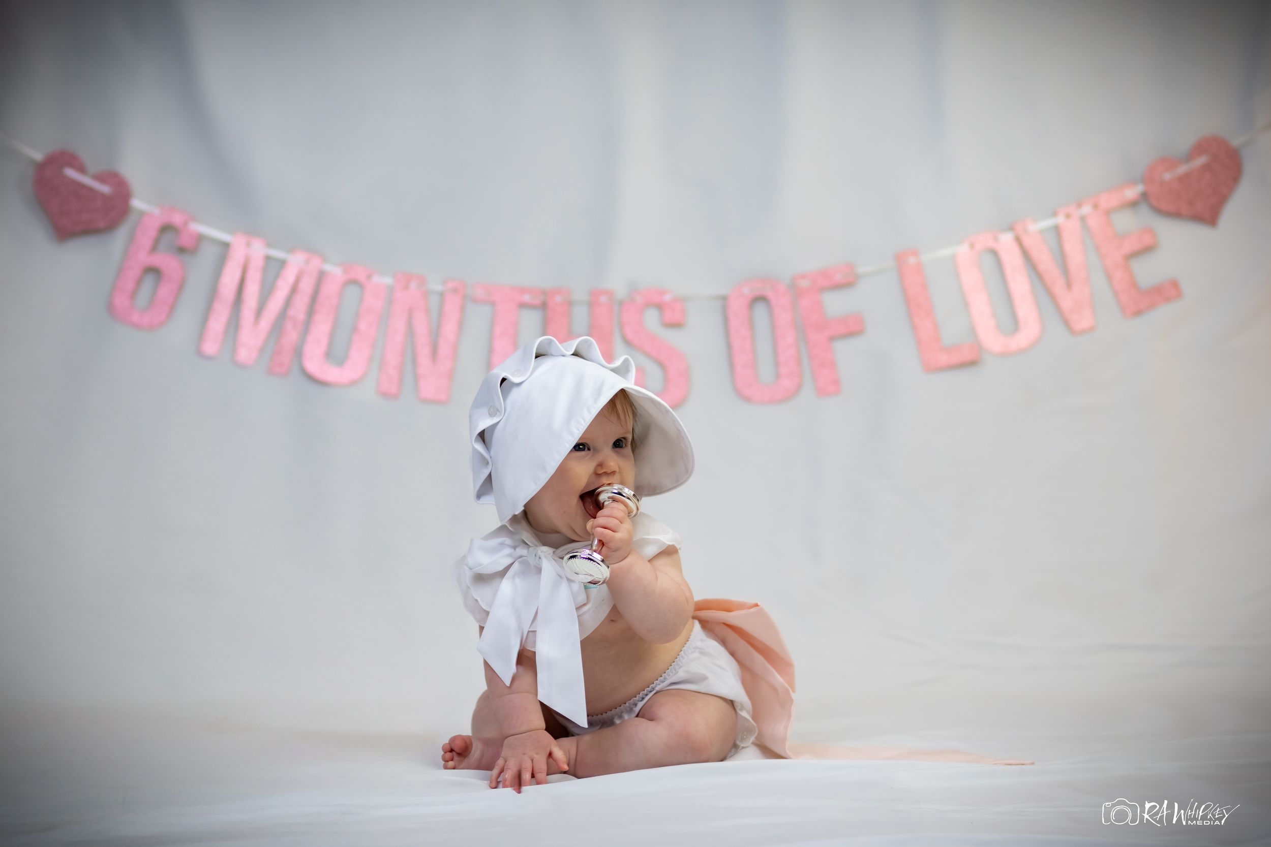 Baby milestone photography session with pink decorative banner.