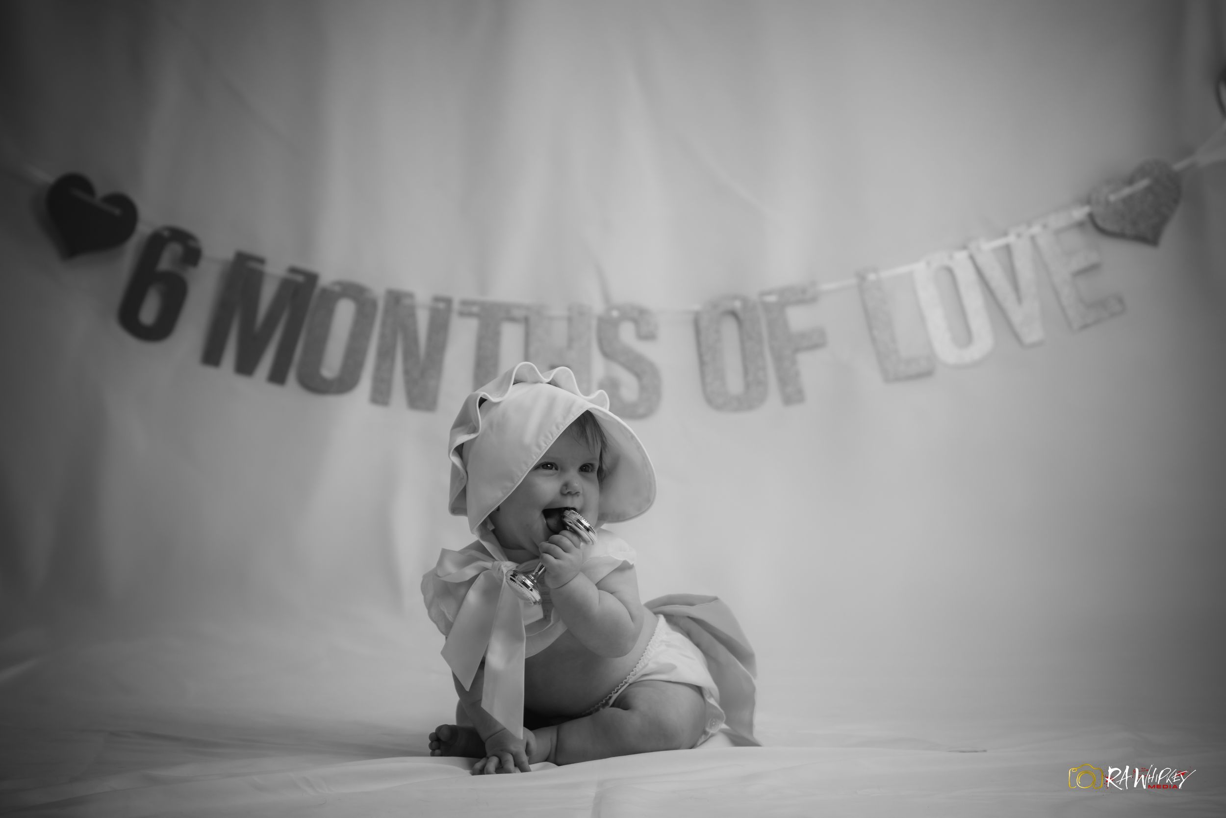 Black and white photo of baby sitting under 6 months banner with heart decorations.
