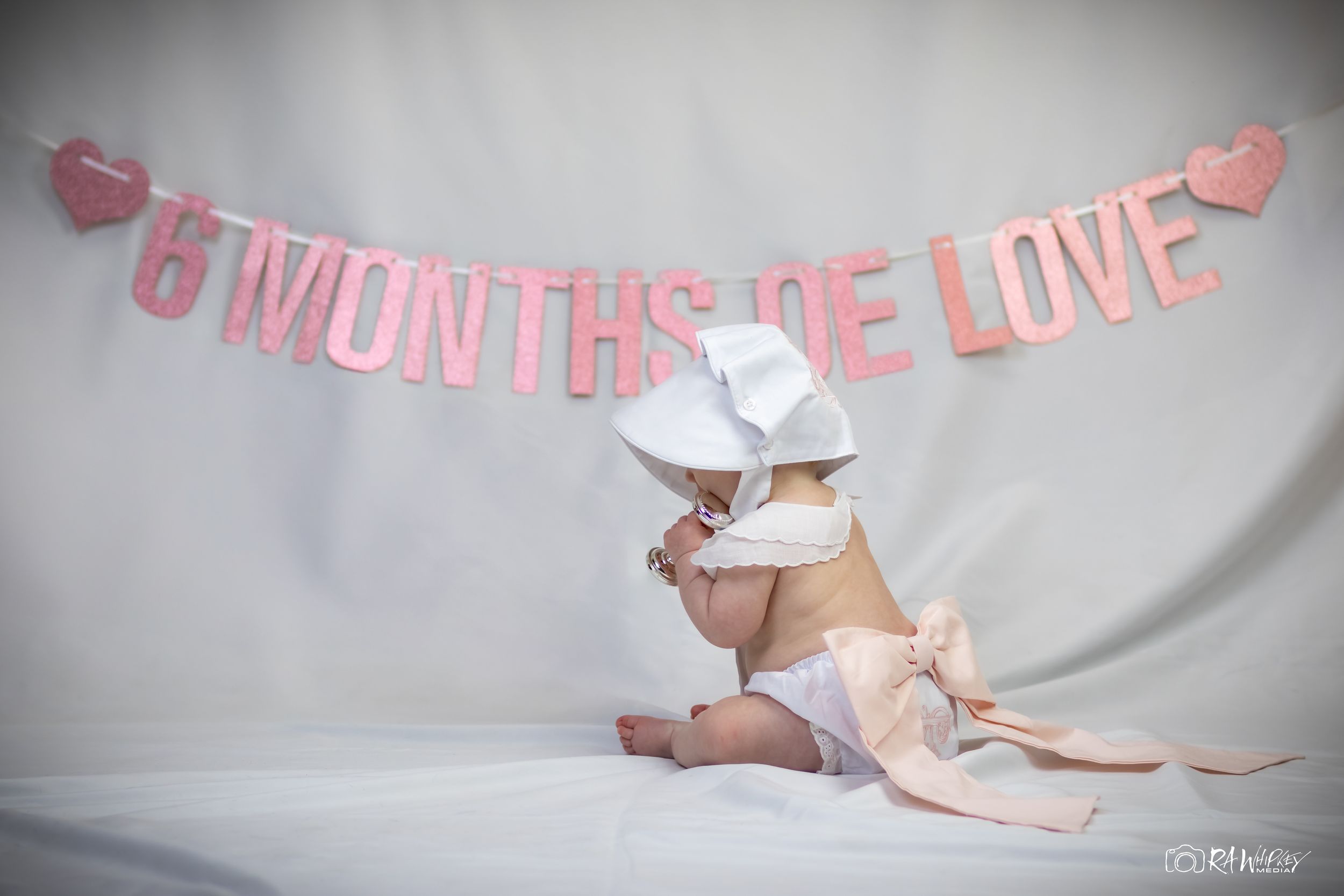 Baby milestone photo with pink decorative banner and white backdrop.