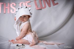 Baby milestone photography with pink lettering backdrop and white hat.