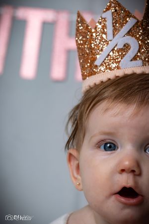 Close up portrait of baby wearing gold crown with surprised expression against blurred background.