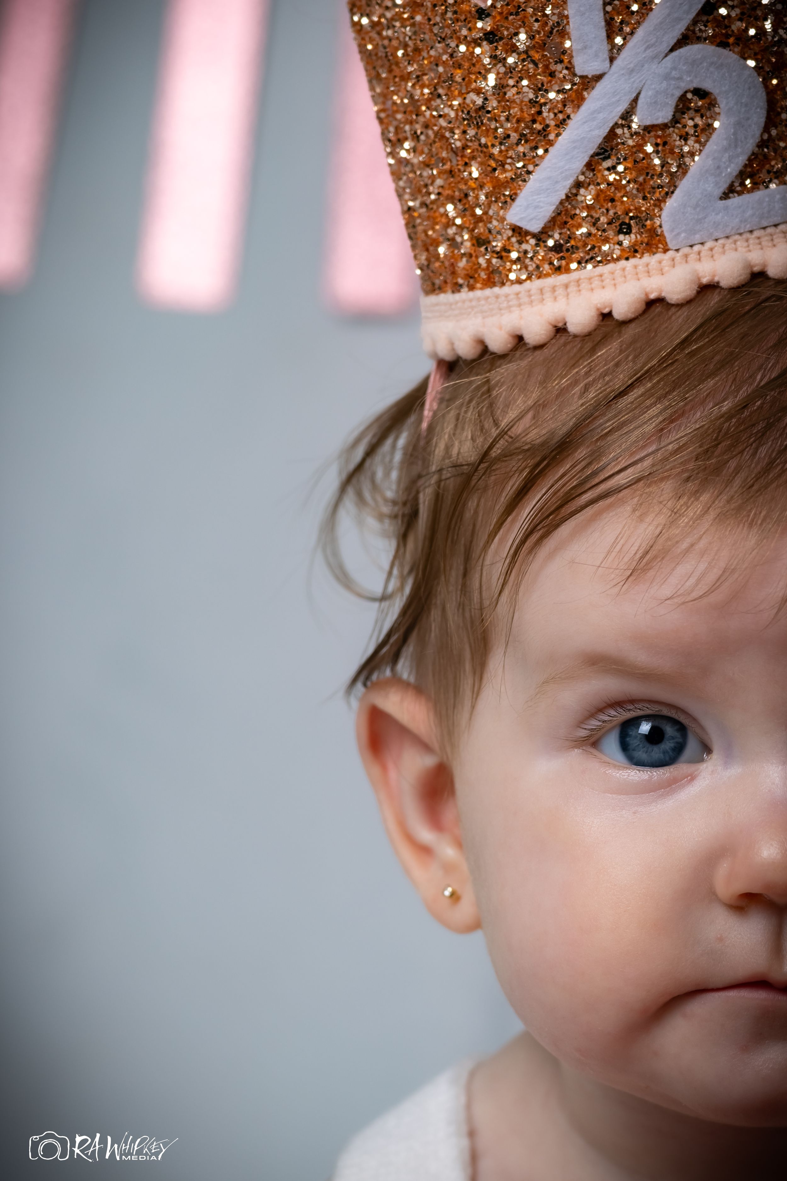 Side profile close up of baby wearing sparkly crown showing blue eye and gold earring.