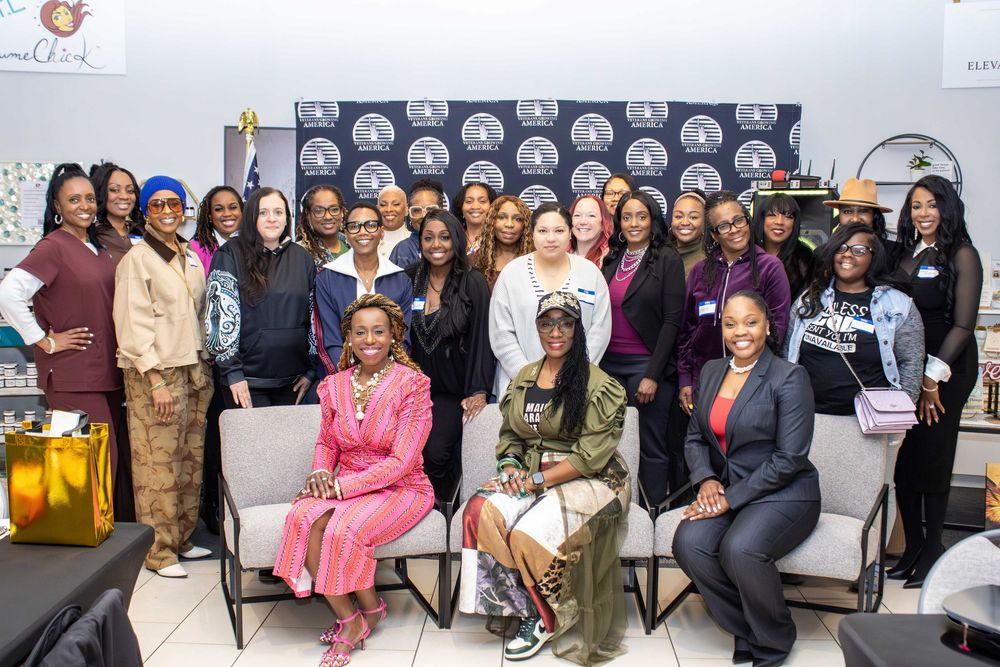 Large group of professional women posing together at a formal networking event in front of a branded backdrop.