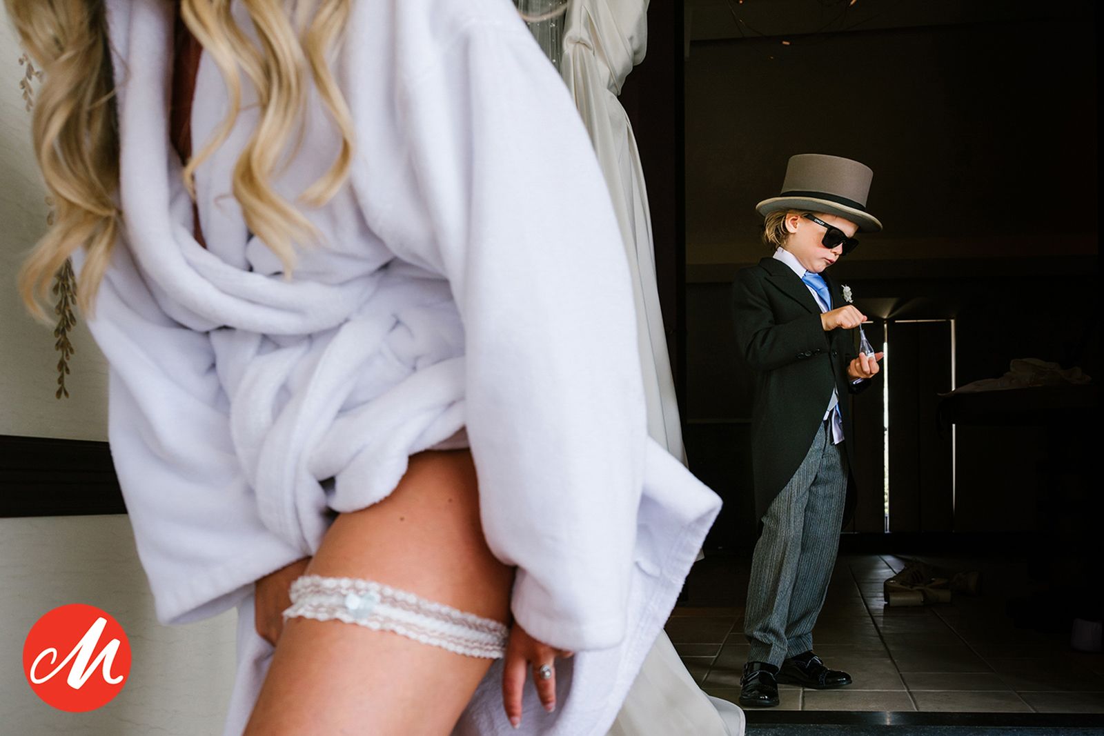 A garter on a bride's leg and a young boy in formal attire with a top hat standing in the shadows.