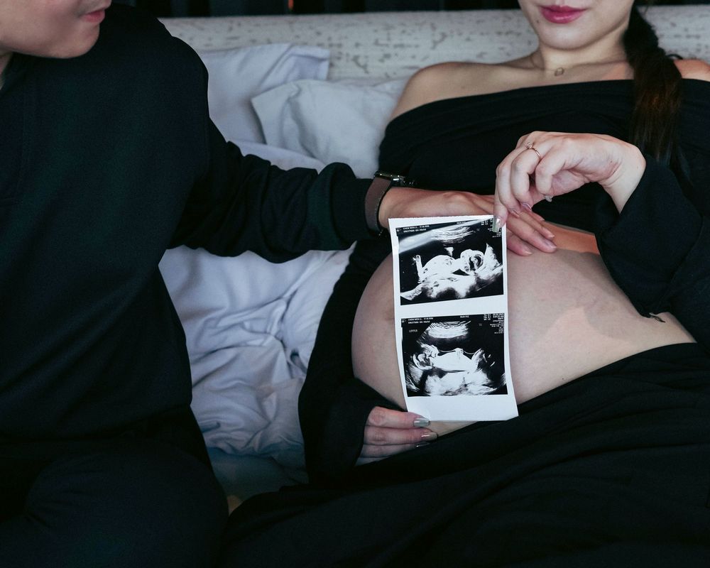 An ultrasound photo is held over a pregnant belly during an intimate maternity session.