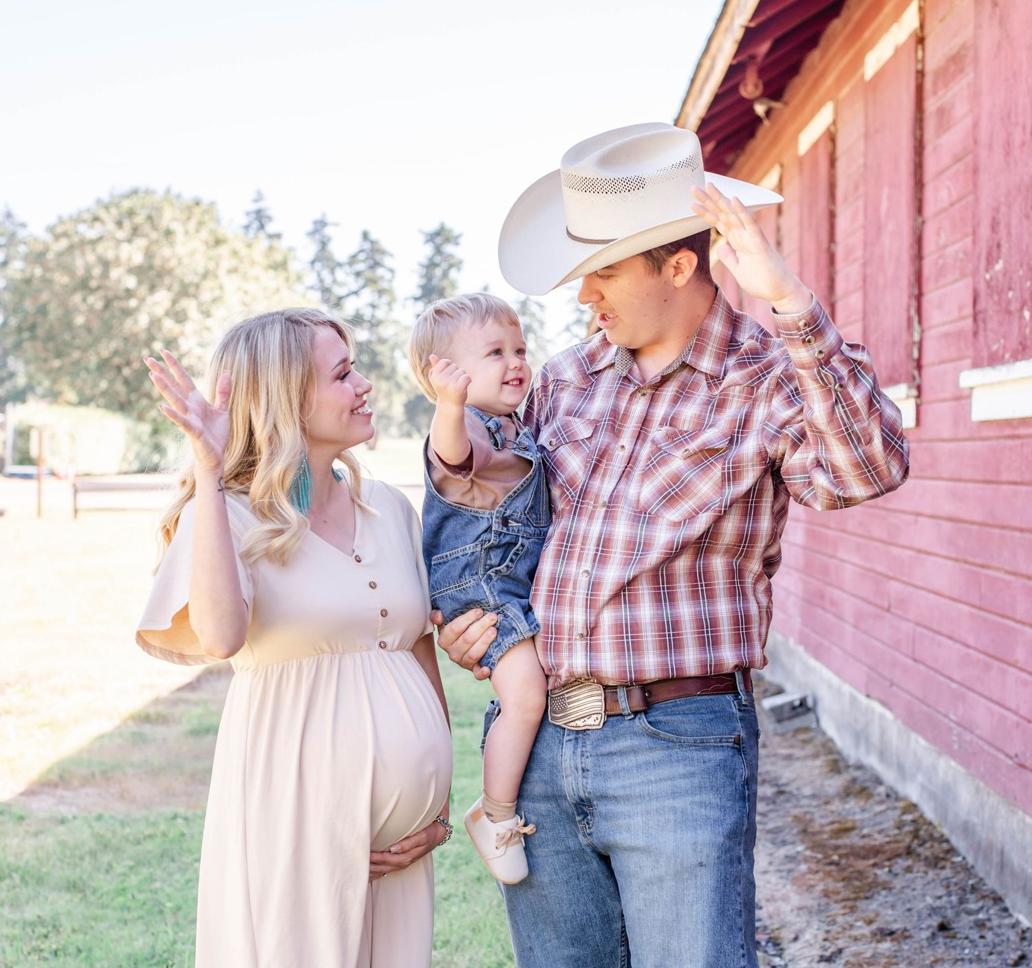 A family poses together against a rustic red barn wearing country western attire in warm afternoon light.