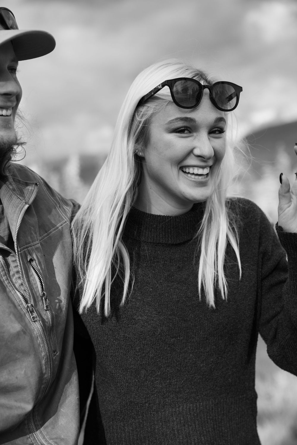 Black and white photo of laughing people outdoors wearing casual attire including sunglasses and a black sweater.