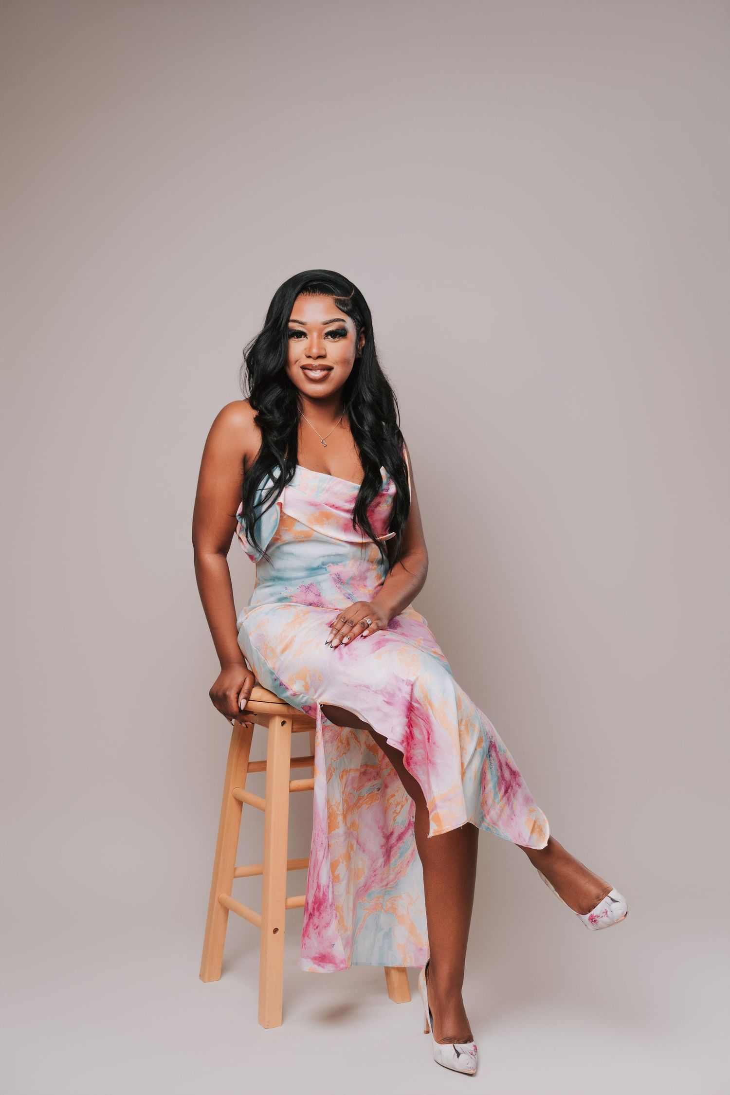 Young woman in a pastel marble-print dress sitting on a wooden stool during a 25th birthday photoshoot at a photo studio in Basildon, Essex