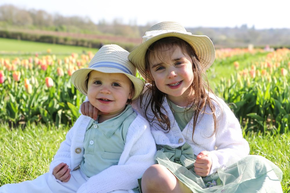 Two children in sun hats sitting together in a blooming tulip field on a sunny spring day.