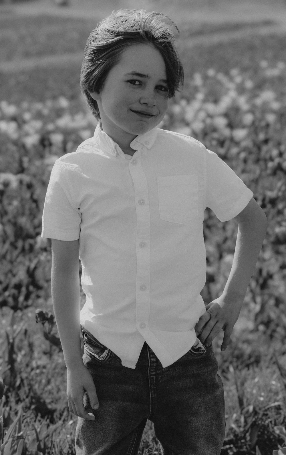 Child in white button-down shirt poses outdoors in black and white portrait against natural background.