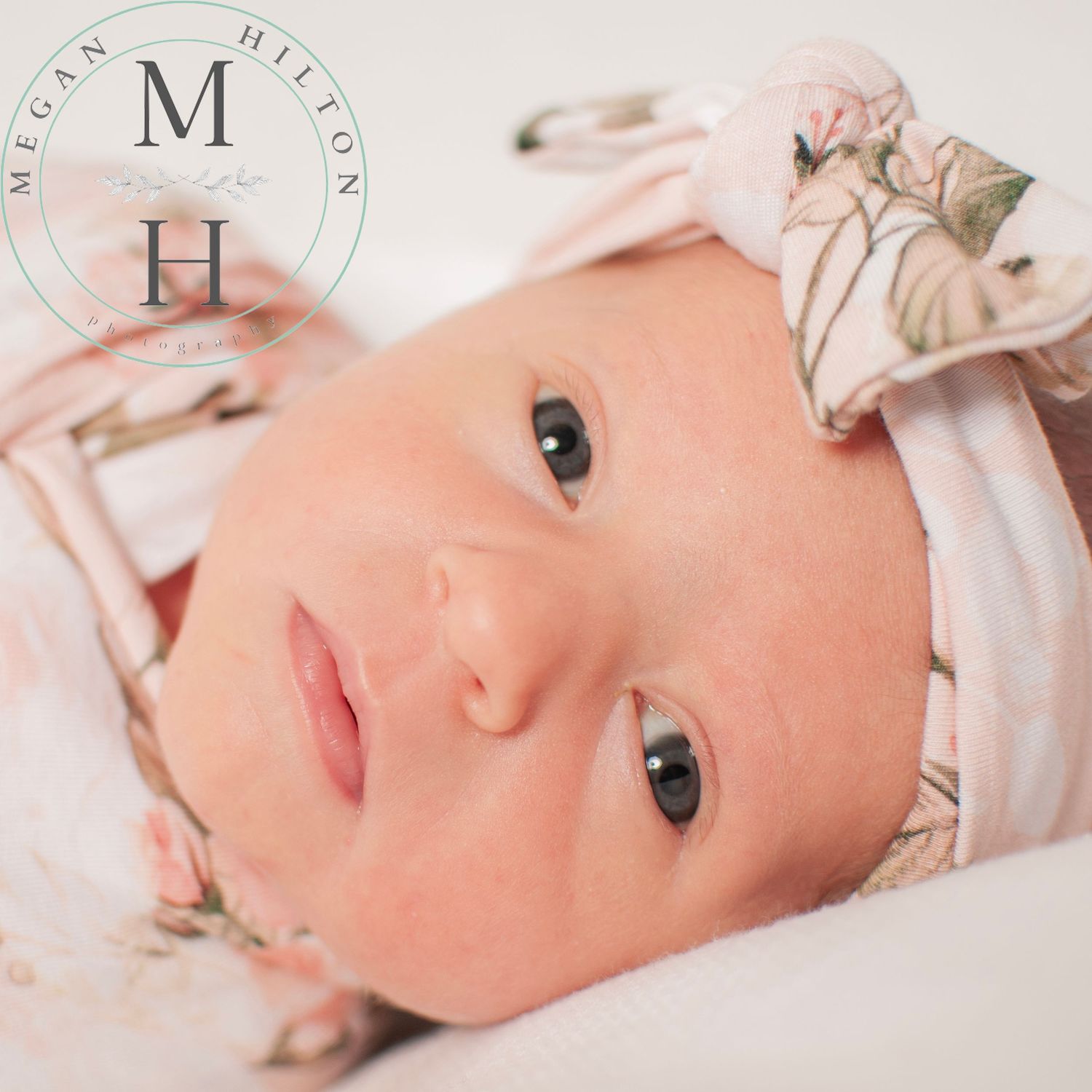 Sweet baby wearing a floral headband lies down while looking at camera with bright eyes.