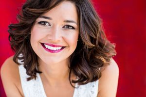 Vibrant portrait with shoulder-length wavy hair and white top against red background.