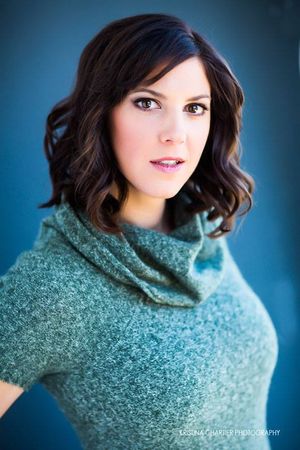 Professional portrait in teal sweater with wavy dark hair against blue background.