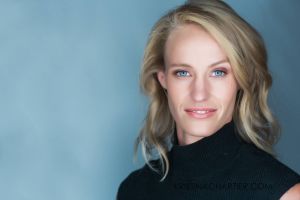 Professional headshot wearing black turtleneck against light blue background.