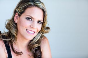 Warm portrait featuring styled blonde waves and natural makeup against light background.