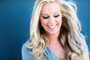 Joyful portrait with flowing blonde hair against blue background wearing gray top.