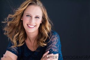 Studio portrait in navy top with wind-swept hair against dark background.
