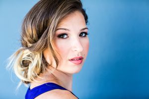Elegant beauty portrait with upswept hairstyle against blue background wearing royal blue top.