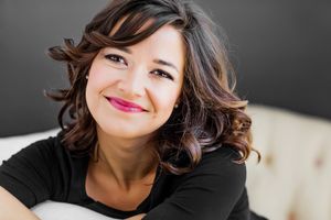 Casual portrait showing wavy brunette hair and bright smile against dark background.