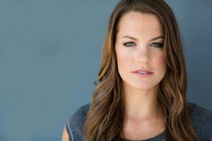 Professional beauty portrait with long brown hair against blue-gray backdrop.