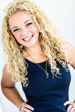 Portrait of person with curly blonde hair wearing navy tank top against white background.