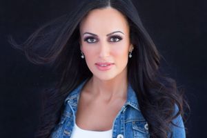 Dramatic portrait in denim jacket against black background with flowing dark hair.