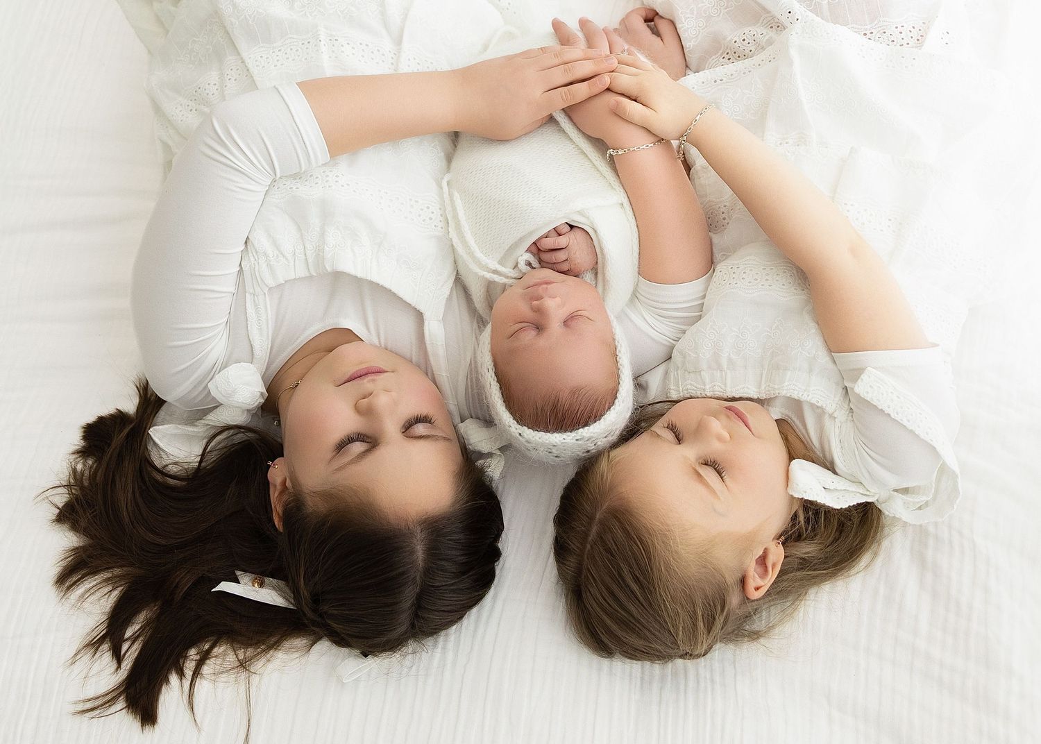 Siblings gather around a white bassinet with pampas grass decoration in a bright minimalist setting.