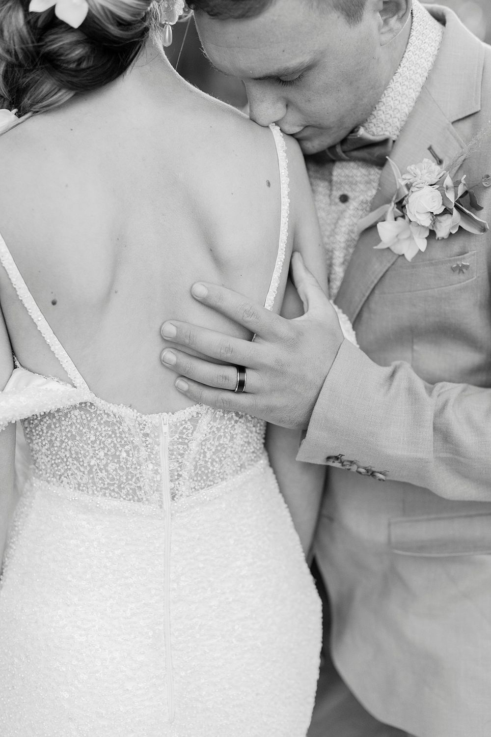 Black and white image of groom kissing bride on her bare back in a delicate backless lace wedding dress.