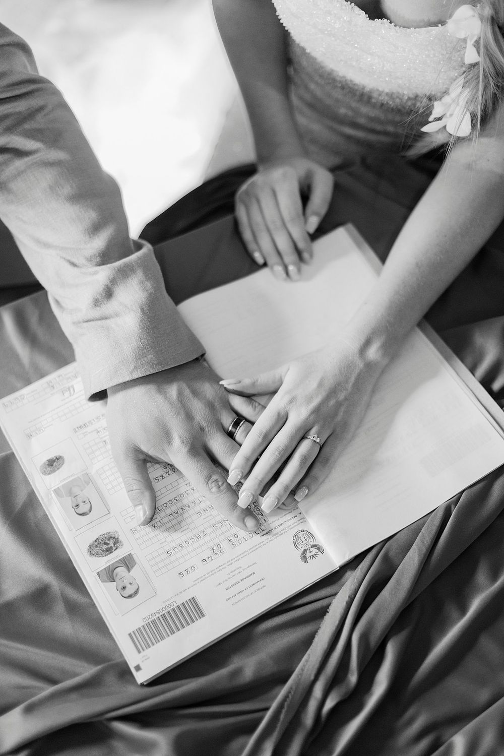 Black and white photo of bride and groom signing wedding registry with rings visible on their hands.