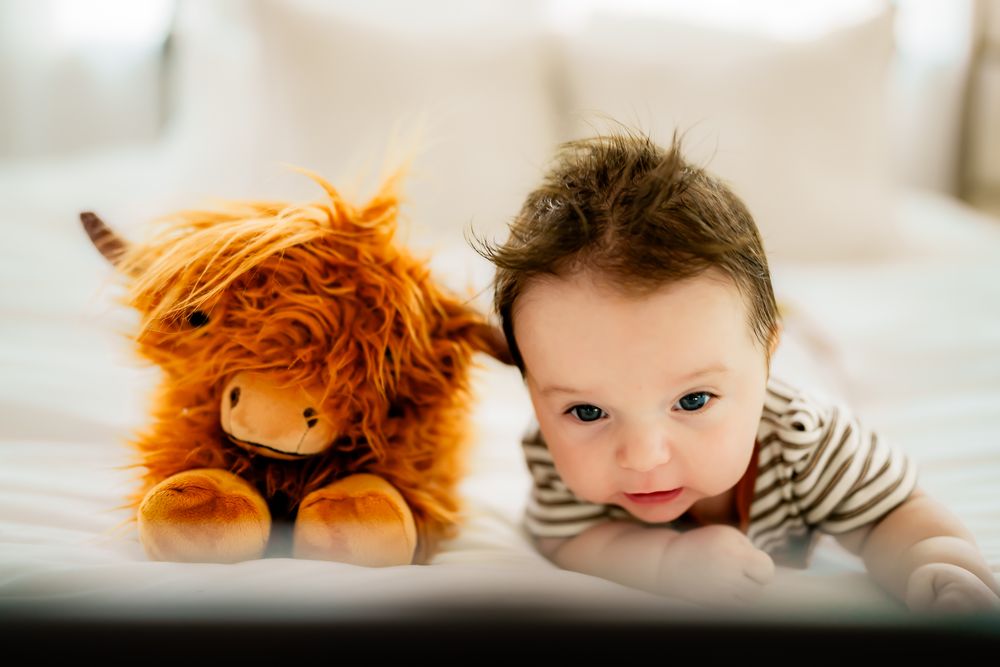 A plush orange lion toy lays beside a young child in a striped shirt on a light colored surface.