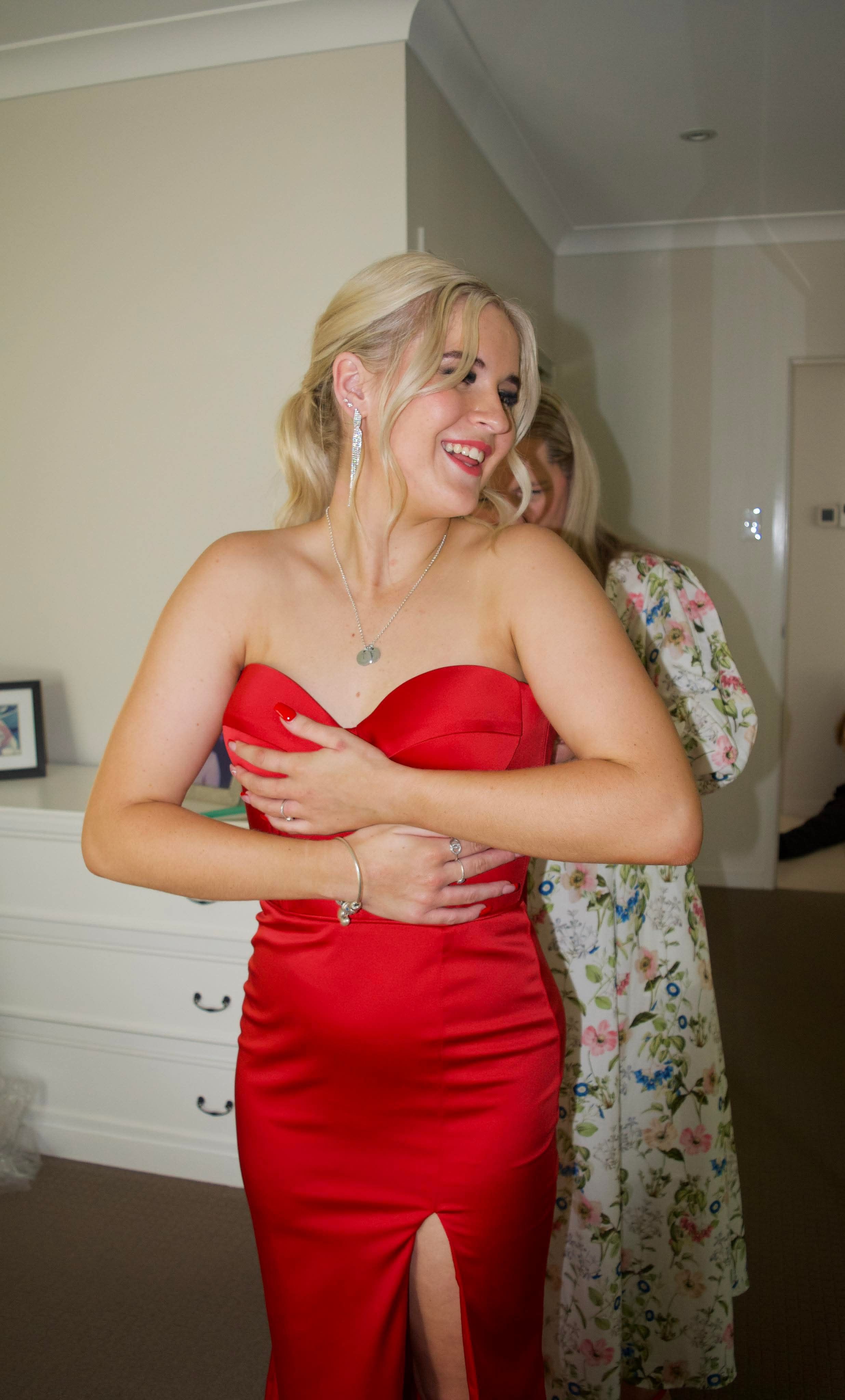 A person wearing a red formal dress poses indoors.