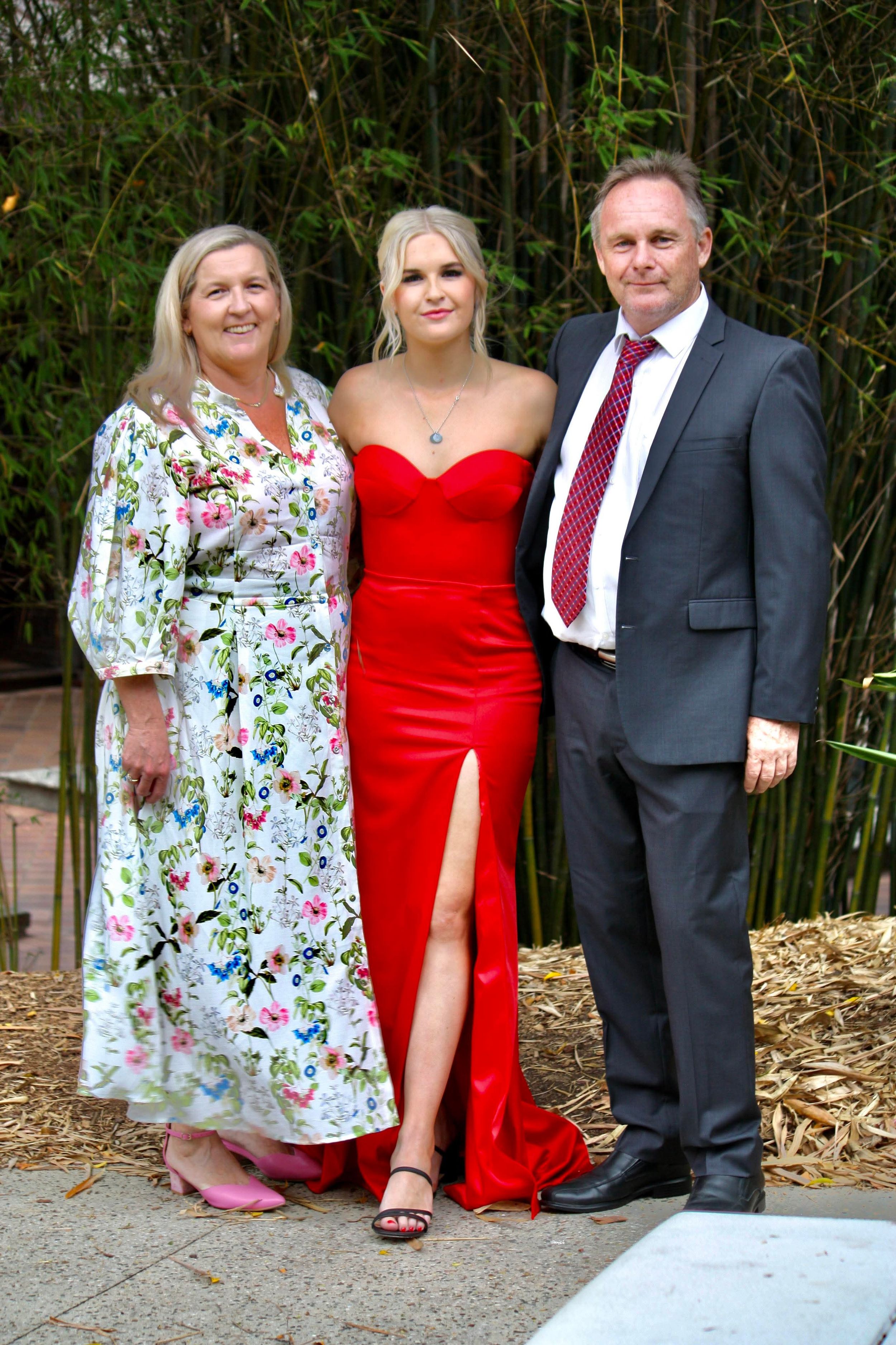 Family photo showing three people dressed formally with bamboo plants in the background.