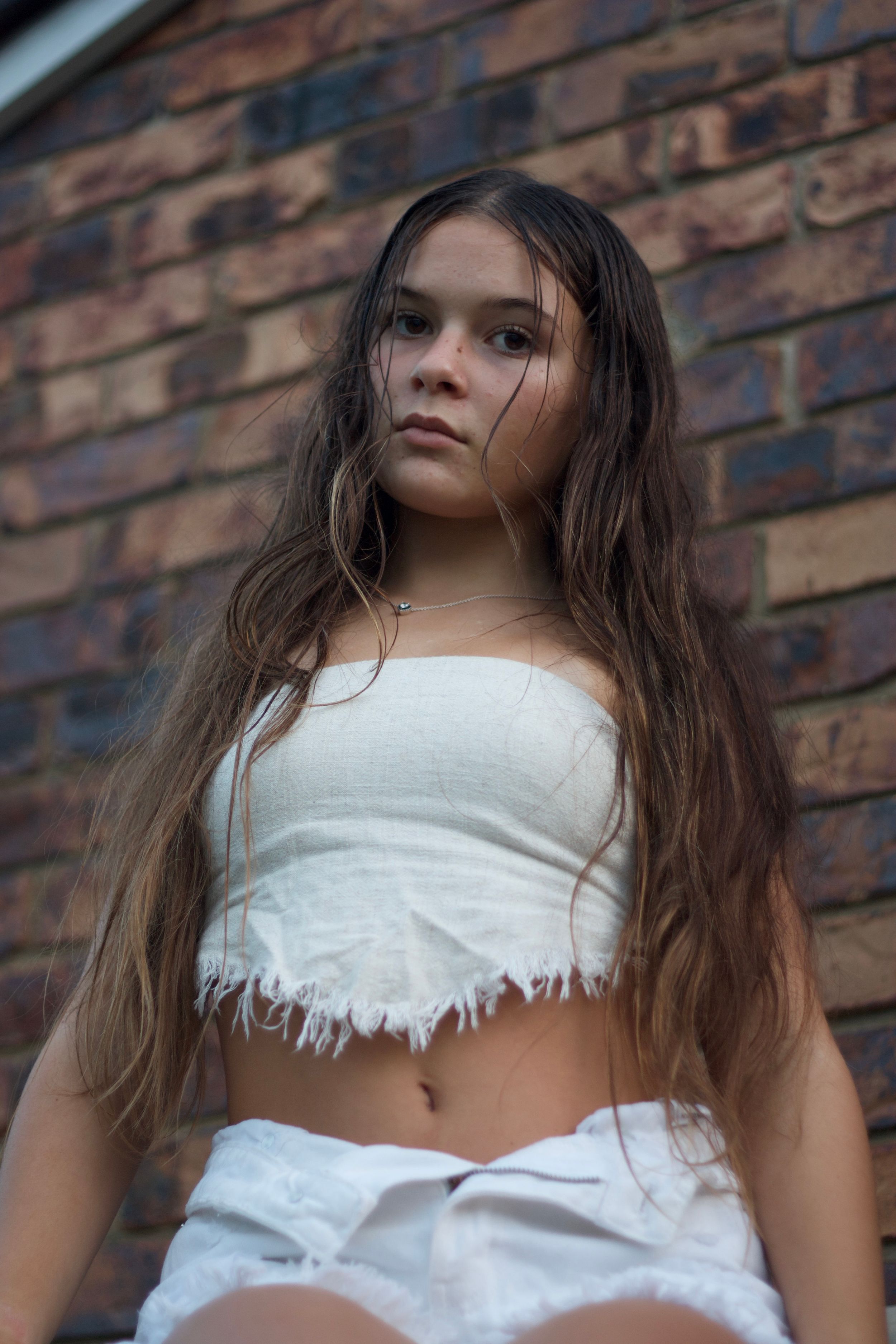 Portrait of young woman in white crop top against brick wall background.