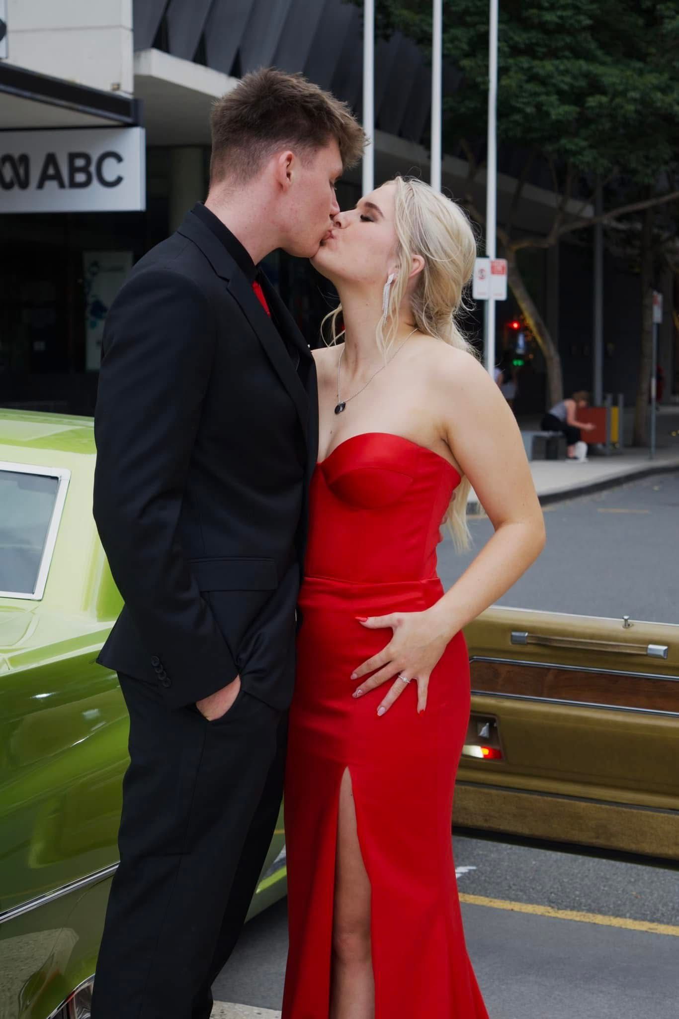 Couple in formal attire sharing a romantic moment next to a vintage car.