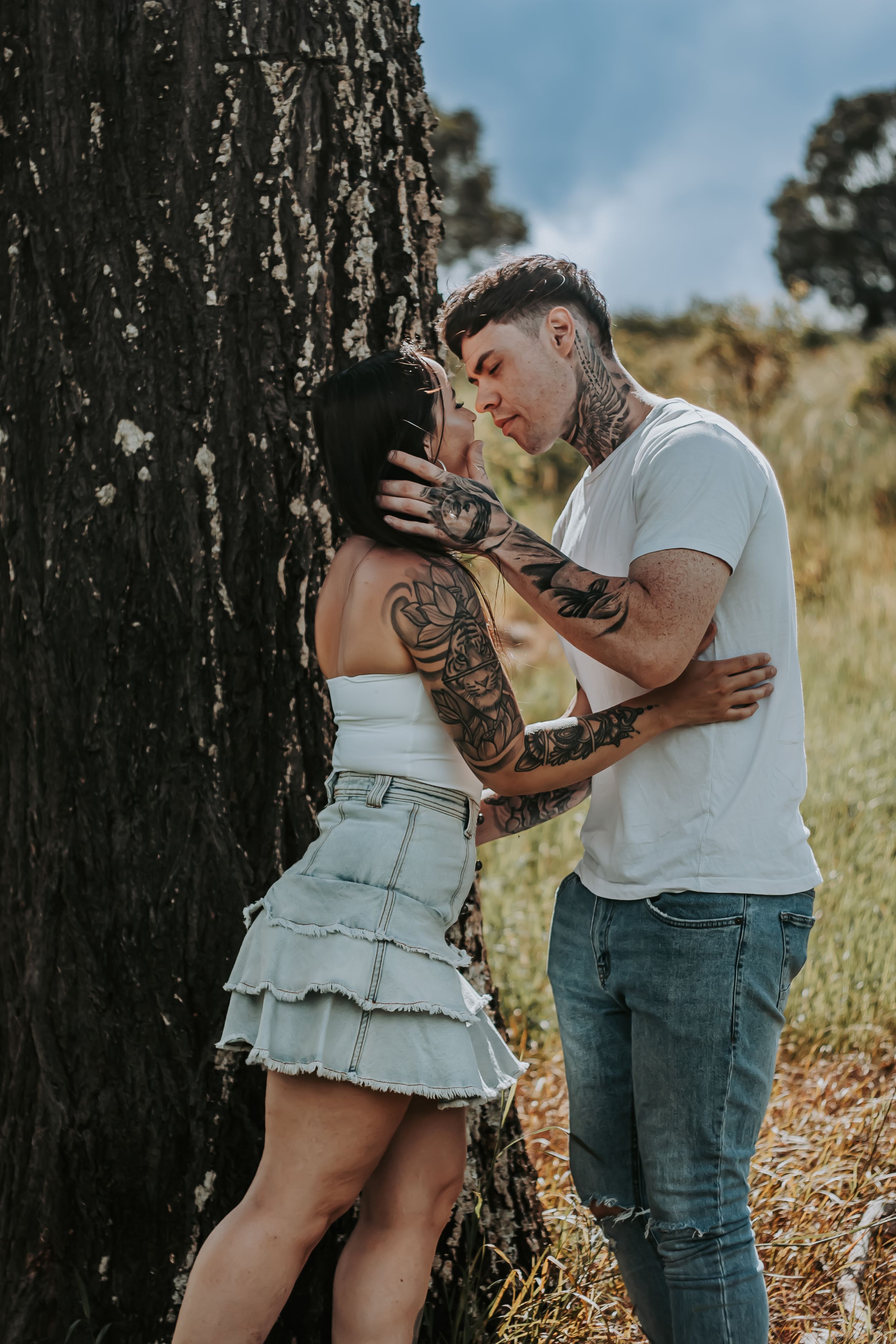 A couple shares an intimate moment against a large tree trunk in nature.