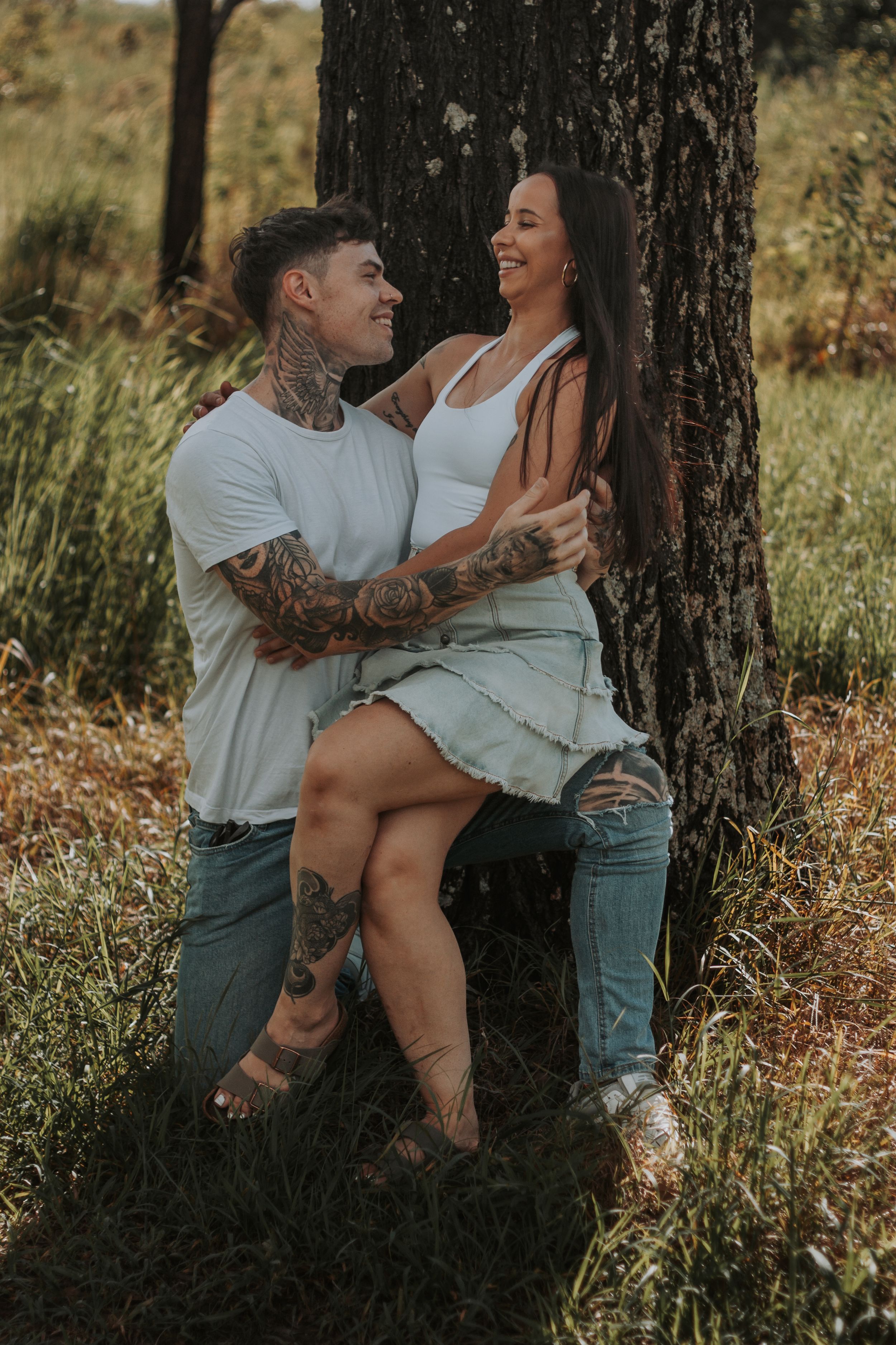 A couple embraces against a tree trunk in a natural outdoor setting.