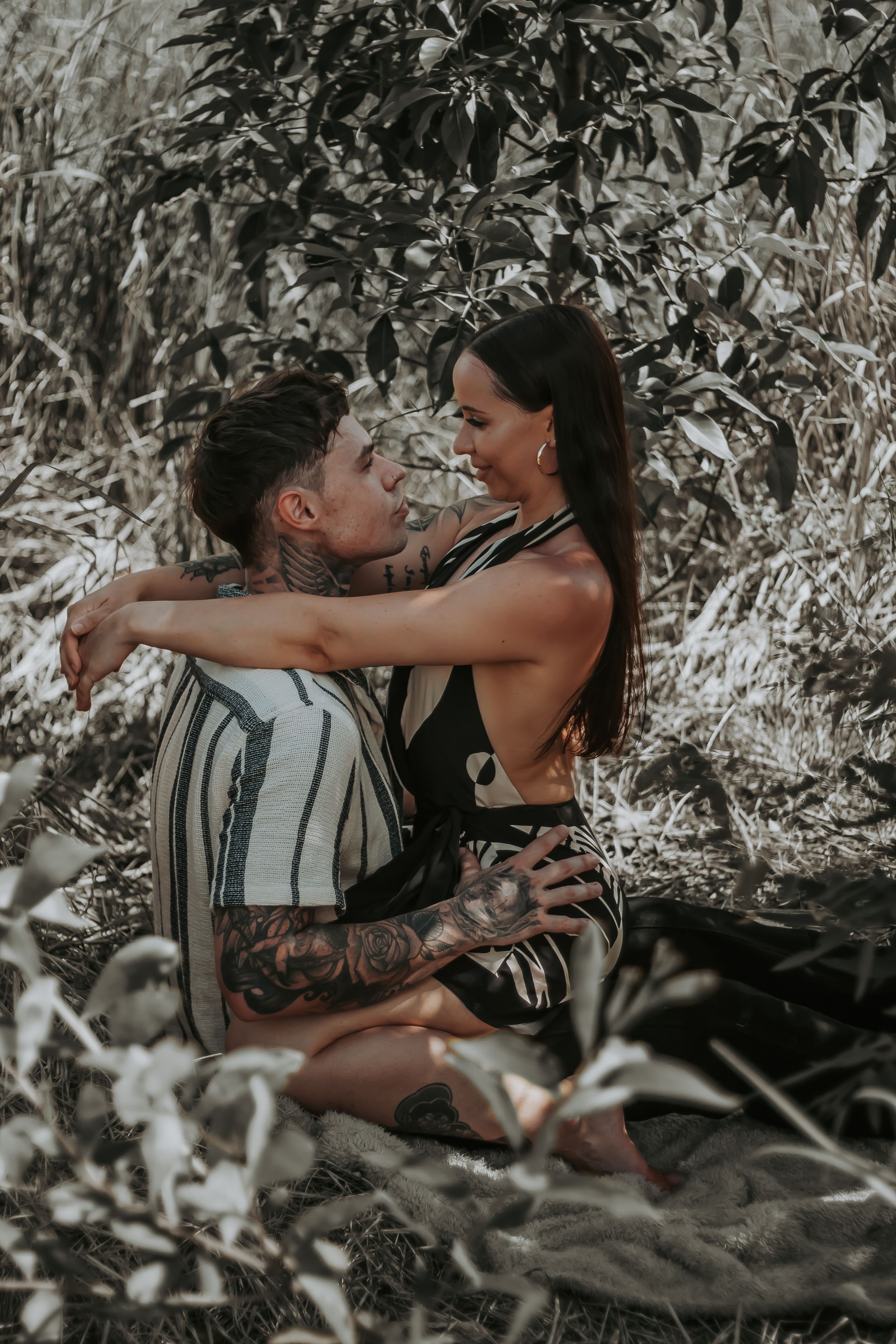 A couple shares an intimate moment among foliage in moody lighting.