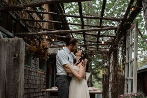 Wedding couple embraces under wooden pergola decorated with twinkle lights.