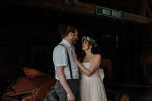 Romantic couple poses against rustic farm equipment in vintage-inspired wedding attire.