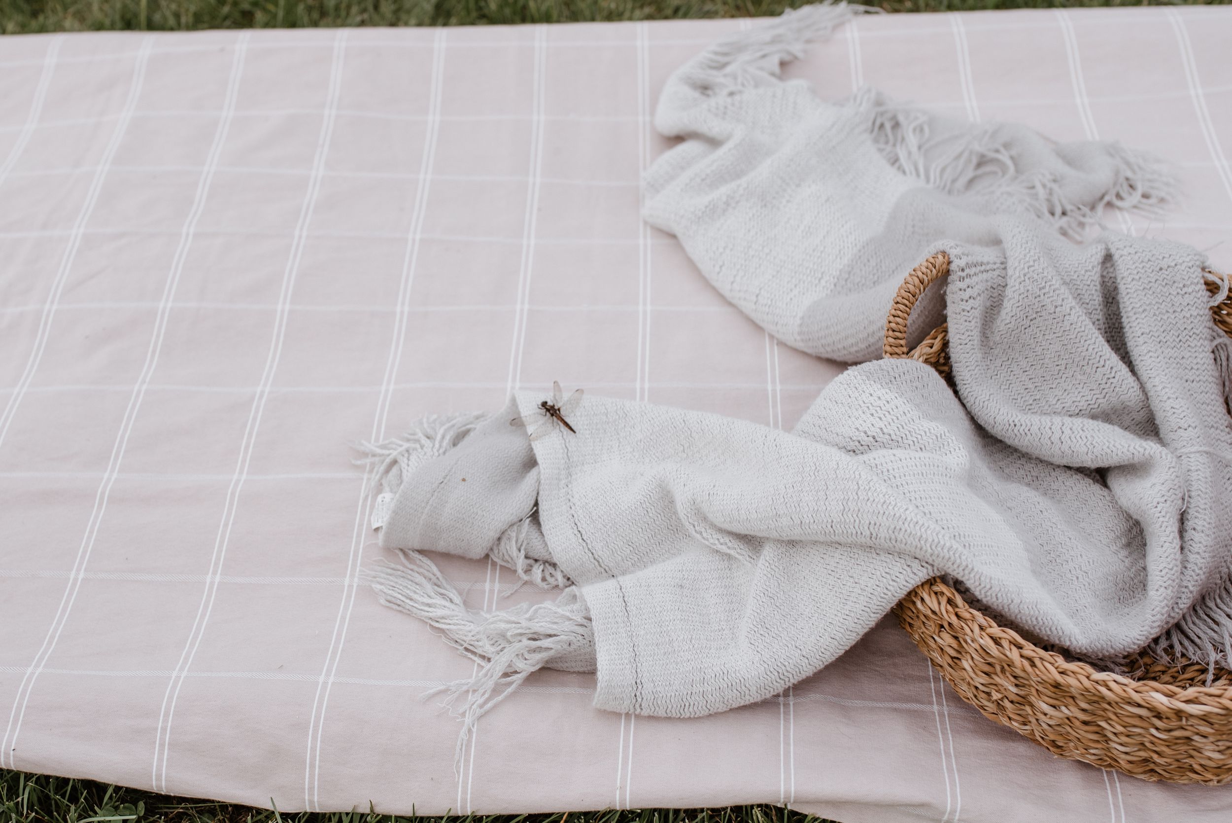 White linen fabric and textiles arranged on blanket with woven basket.