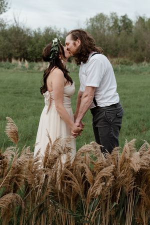 A romantic couple poses together in a field of tall wheat, surrounded by nature on their wedding day.