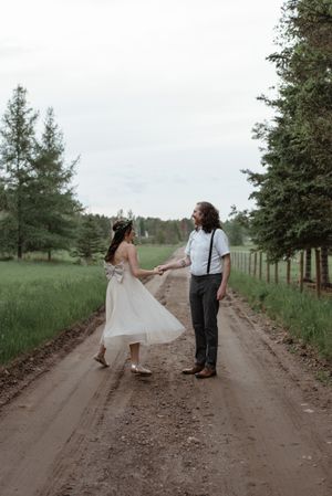 A couple in wedding attire dances together on a tree-lined country road.
