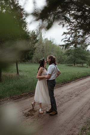 A romantic moment between a couple on a dirt road surrounded by lush green trees.