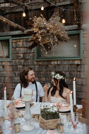 A romantic candlelit dinner table setting with hanging lights and dried floral decorations.