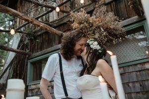 An intimate moment between newlyweds under dried flower decorations near a rustic building.