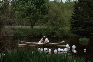 A couple shares an intimate moment in a rowboat surrounded by floating lanterns on a pond.